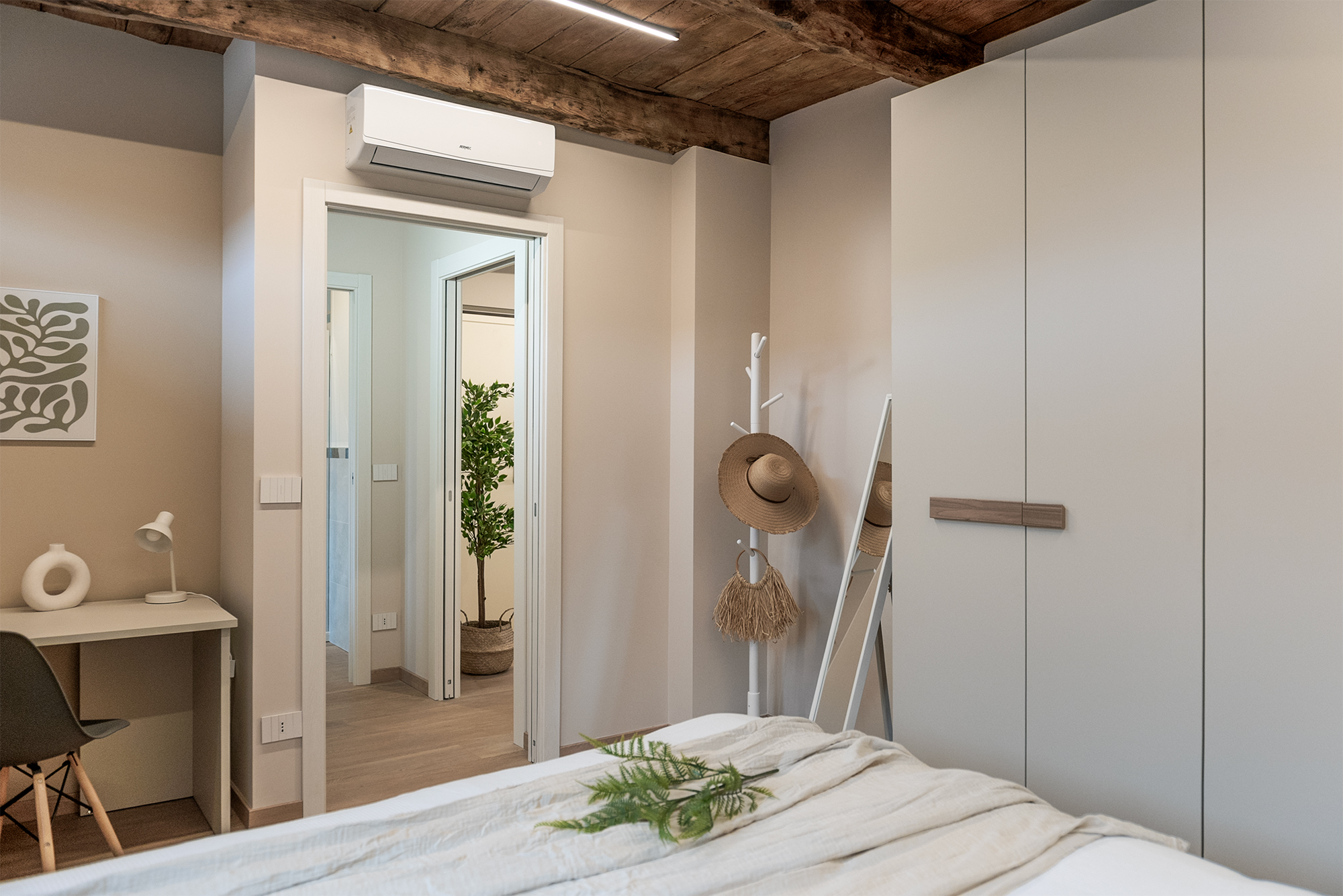 La camera matrimoniale nei toni del bianco, con armadio e aria condizionata La cucina con basi e frigo blu e pensili bianchi, travi a vista e tavolo da pranzo rotondo bianco nel bilocale in affitto a Savigliano Schiaparelli