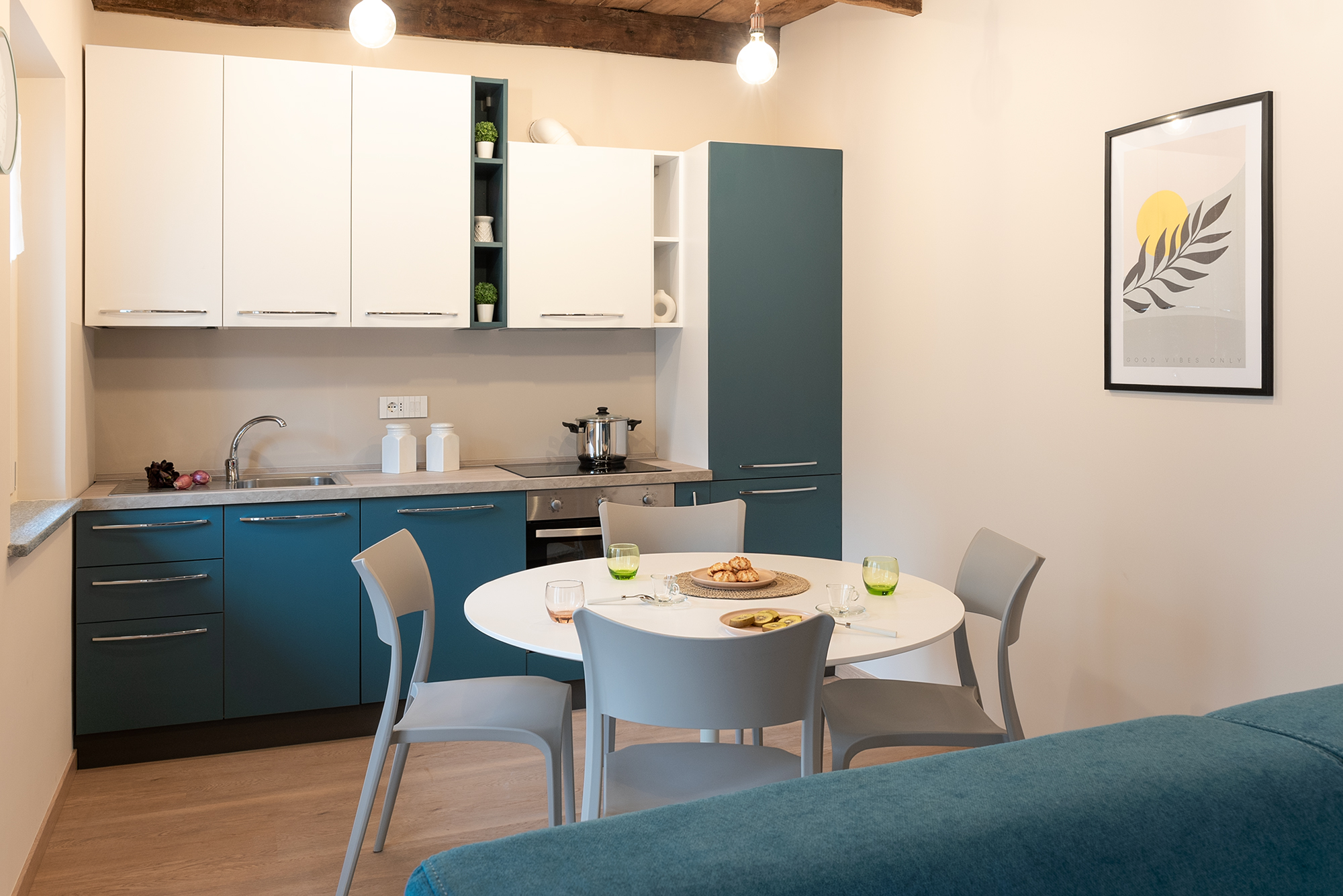 La cucina con basi e frigo blu e pensili bianchi, travi a vista e tavolo da pranzo rotondo bianco nel bilocale in affitto a Savigliano Schiaparelli