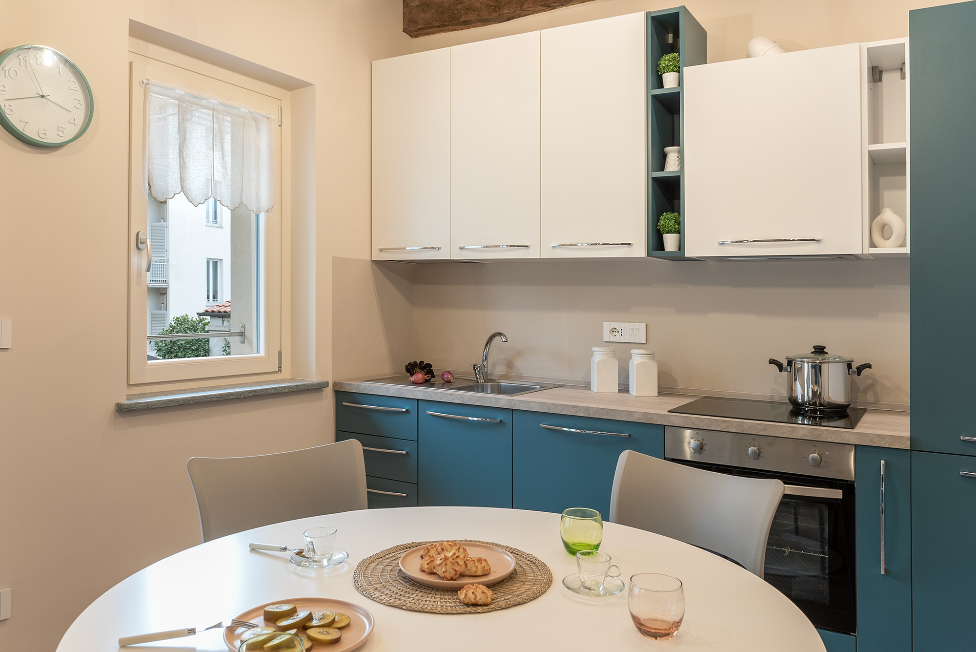 La cucina con basi e frigo blu e pensili bianchi, travi a vista e tavolo da pranzo rotondo bianco nel bilocale in affitto a Savigliano Schiaparelli