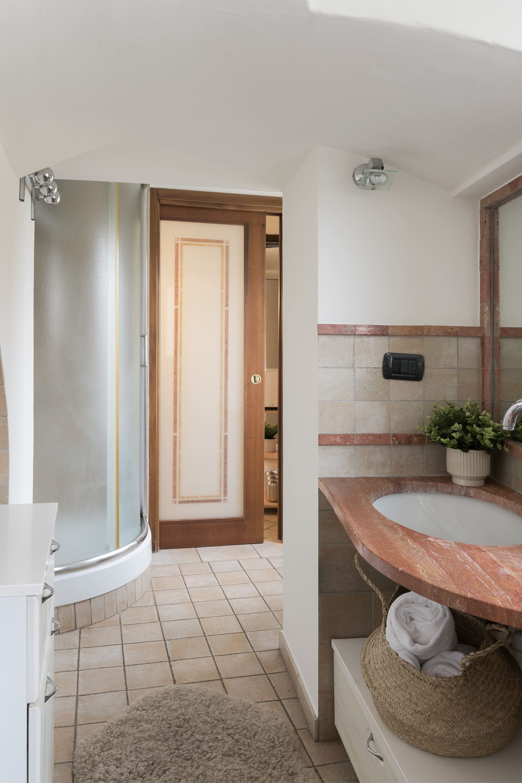 Il bagno: la porta in vetro satinato, il lavabo sospeso e incassato nel marmo rosa e la doccia