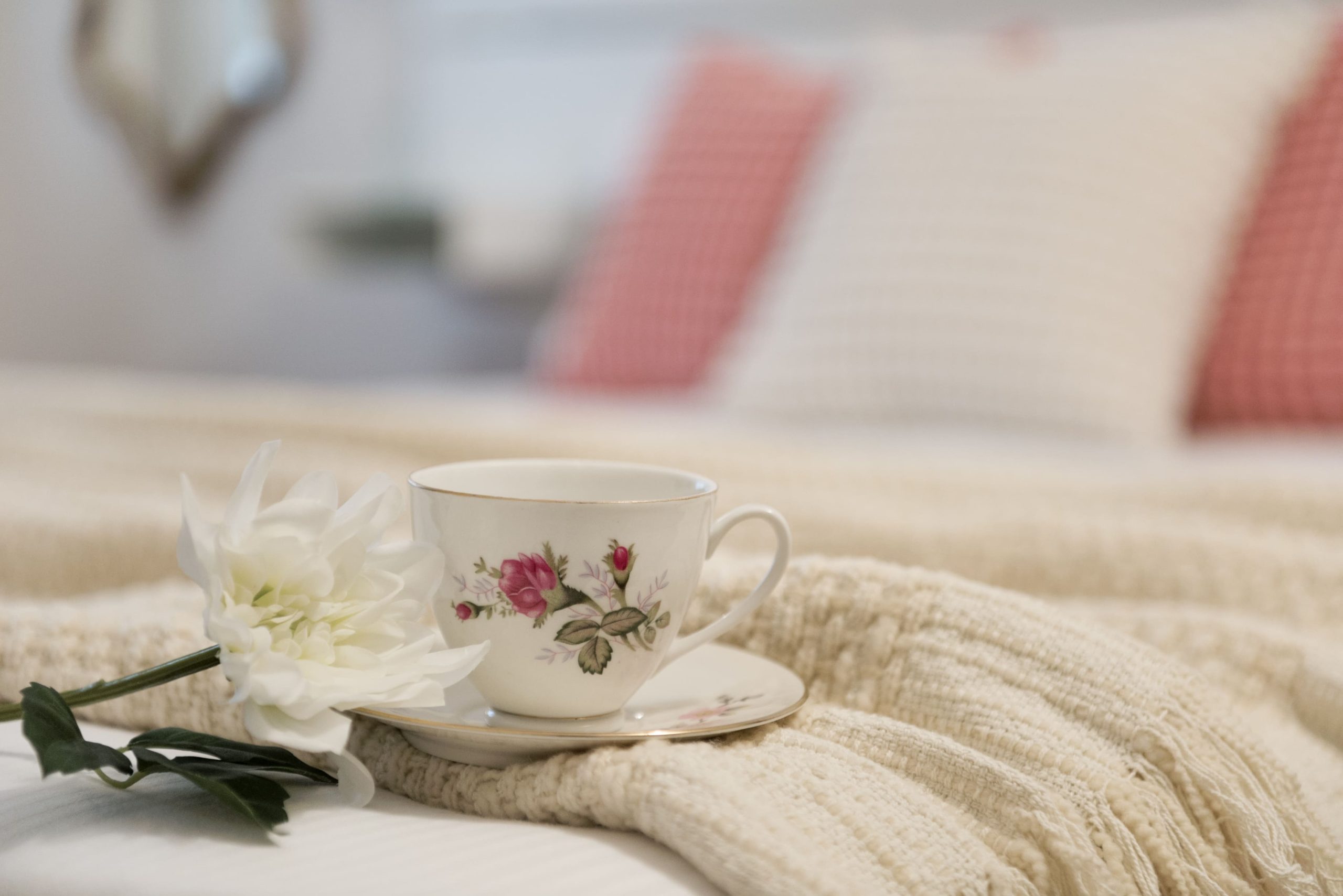 Il dettaglio di una tazza da te bianca con roselline appoggiato al letto