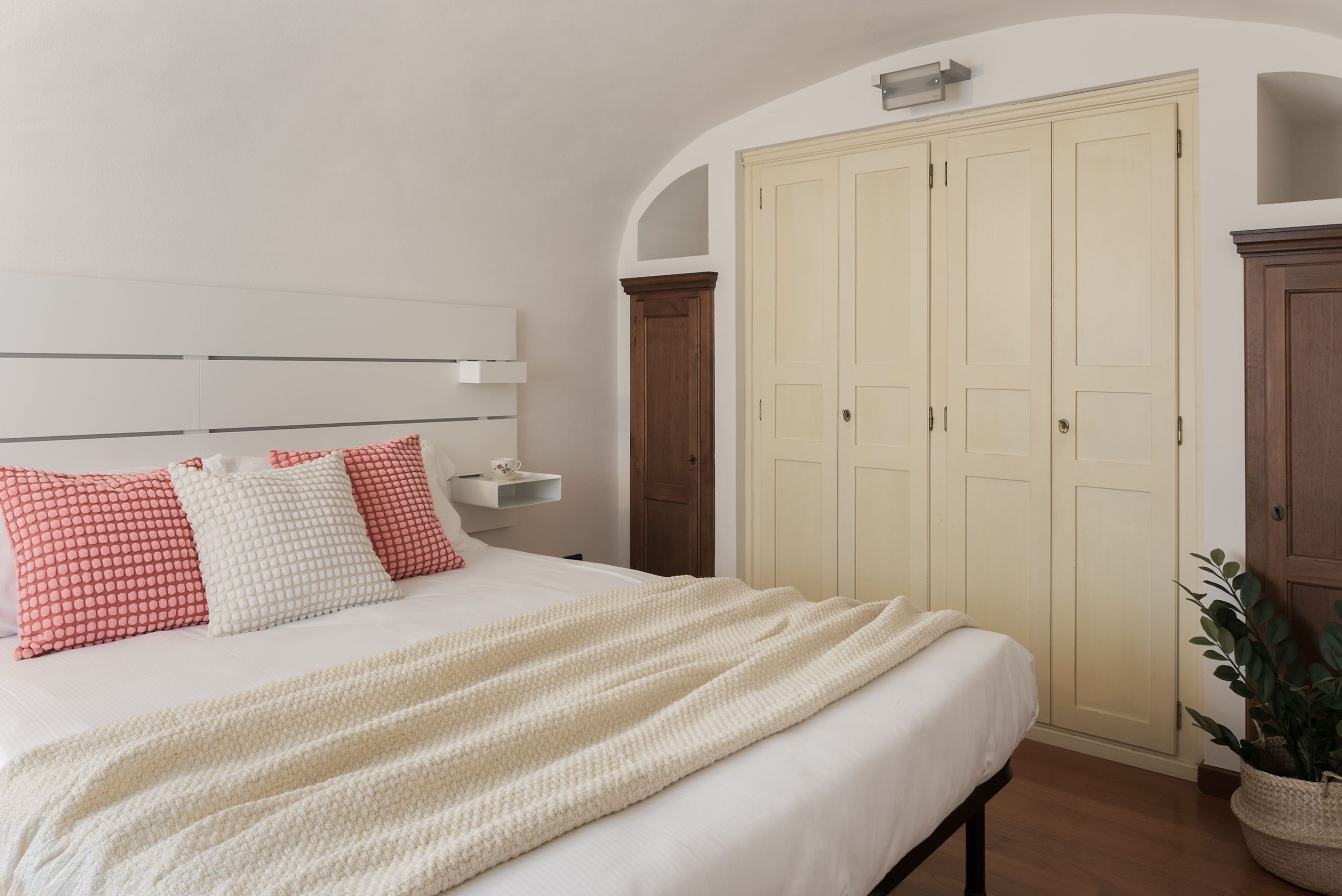 Il letto nei toni del panna e del rosa e, accanto, l'armadio in legno bianco incassato nel muro