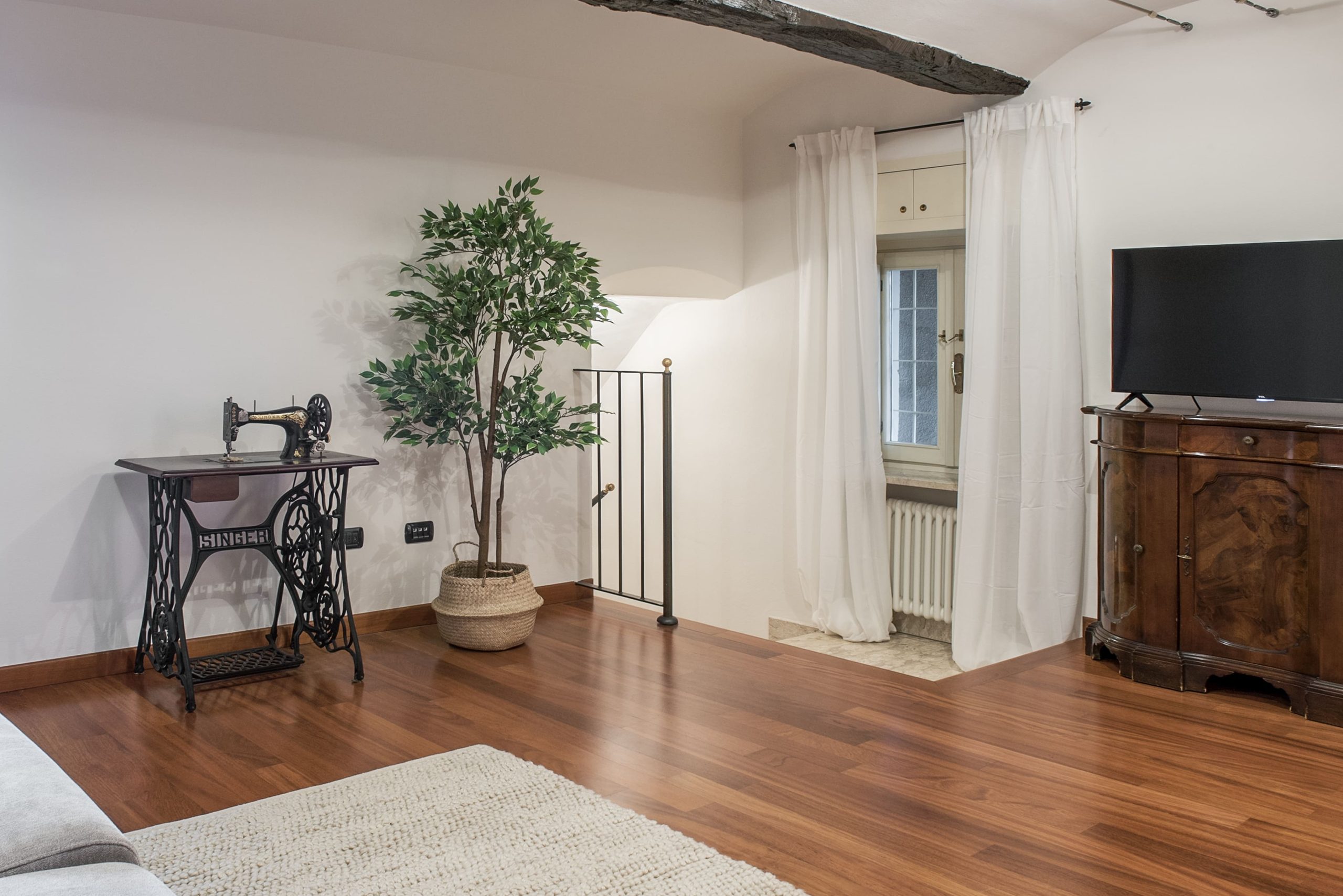 Il salotto con parquet, macchina da cucire Singer anni 50 mobile tv e travi a vista nella casa in affitto a Savigliano