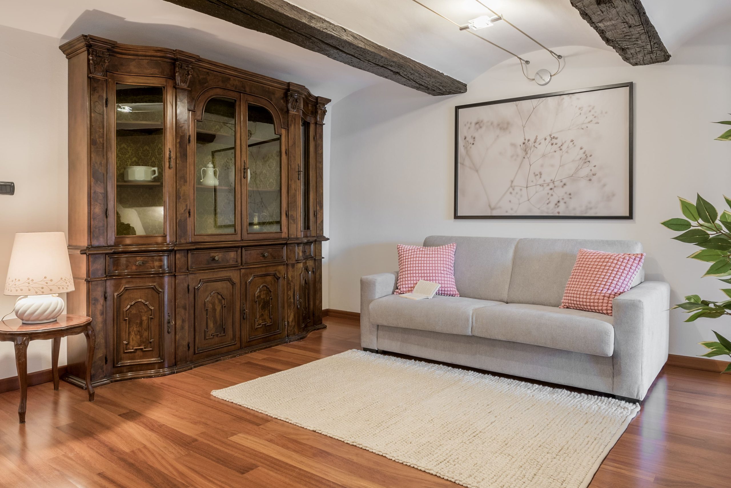 Il salotto con divano grigio, parquet, credenza antica in legno, travi a vista nella casa in affitto a Savigliano