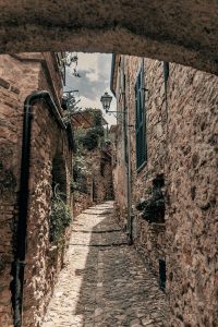 Glimpse of Colla Micheri. A narrow and paved alley climbs the hill. All around are ancient houses with a stone facade.