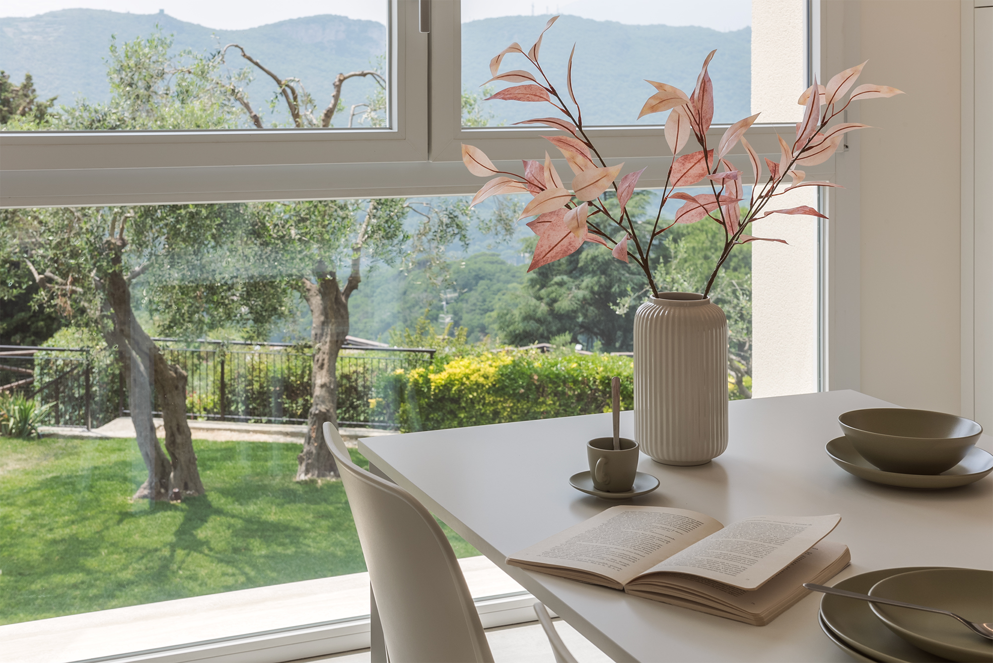 Un dettaglio del tavolo della cucina con piatti e un vaso con fiori che affaccia sul verde del giardino della casa vacanza a Finale Ligure
