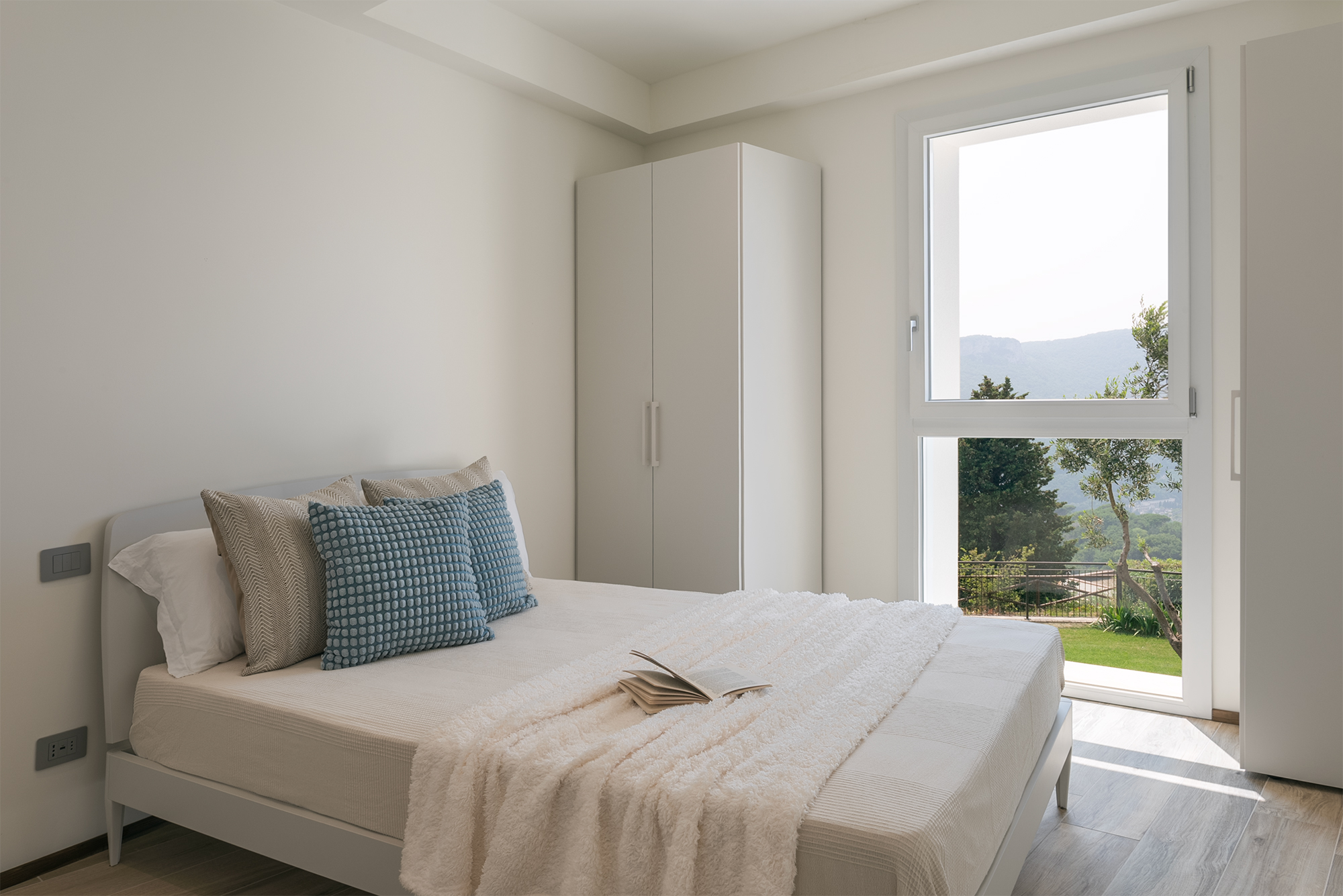 Il letto matrimoniale nella seconda camera con armadio a due ante e grande finestra sul verde della casa vacanza a Finale Ligure